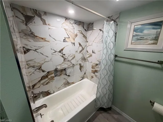 Bathtub and shower combination featuring large format marble-look wall tiles, brushed nickel fixtures, and a recessed ceiling light