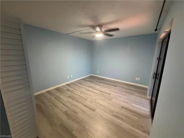 Spacious room featuring light blue walls, wood-finish flooring, and white baseboards