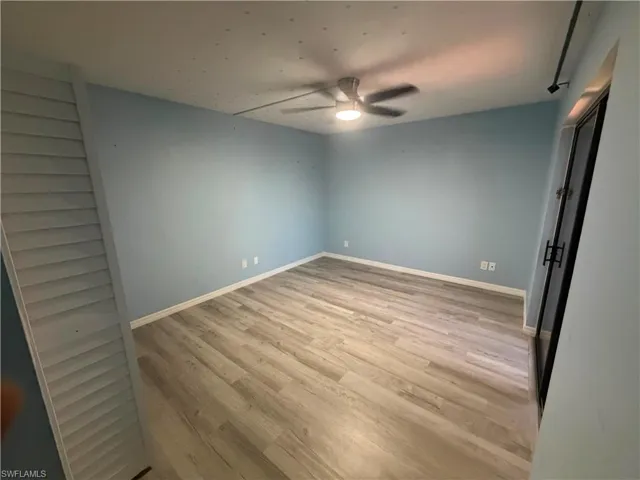 Spacious room featuring light blue walls, wood-finish flooring, white baseboards, and a ceiling fan with integrated lighting