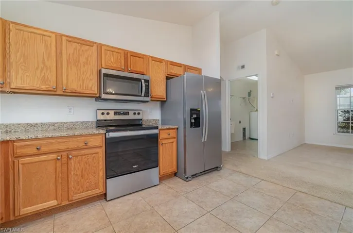 Kitchen with vaulted ceiling, stainless steel appliances, light stone counters, and light tile patterned flooring