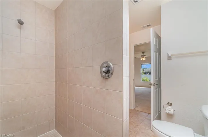 Bathroom with ceiling fan, toilet, and tiled shower