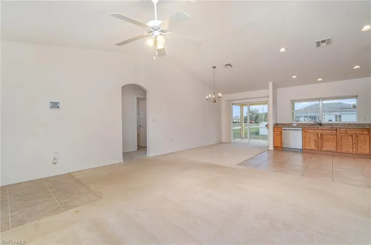 Unfurnished living room featuring ceiling fan with notable chandelier, sink, lofted ceiling, and light carpet