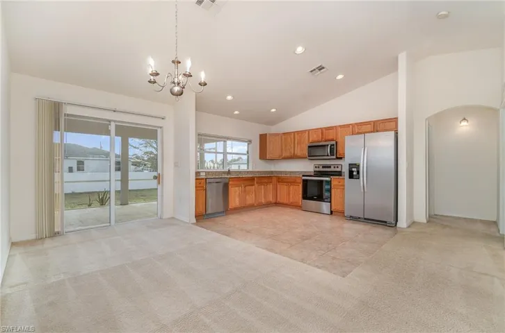 Kitchen featuring stainless steel appliances, light colored carpet, pendant lighting, high vaulted ceiling, and a notable chandelier