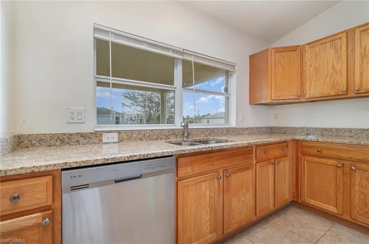 Kitchen featuring dishwasher, lofted ceiling, sink, light stone countertops, and light tile patterned flooring