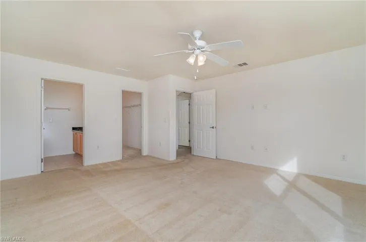 Unfurnished bedroom with a walk in closet, ensuite bath, ceiling fan, light colored carpet, and a closet