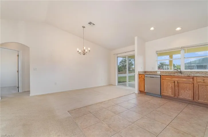 Kitchen with an inviting chandelier, hanging light fixtures, vaulted ceiling, stainless steel dishwasher, and light colored carpet