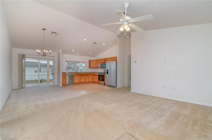 Unfurnished living room with light carpet, ceiling fan with notable chandelier, and high vaulted ceiling