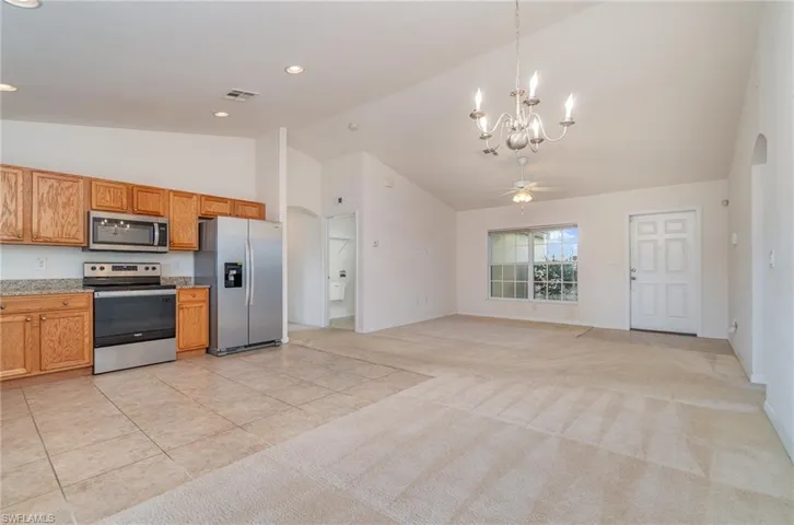 Kitchen with pendant lighting, lofted ceiling, light carpet, ceiling fan with notable chandelier, and appliances with stainless steel finishes