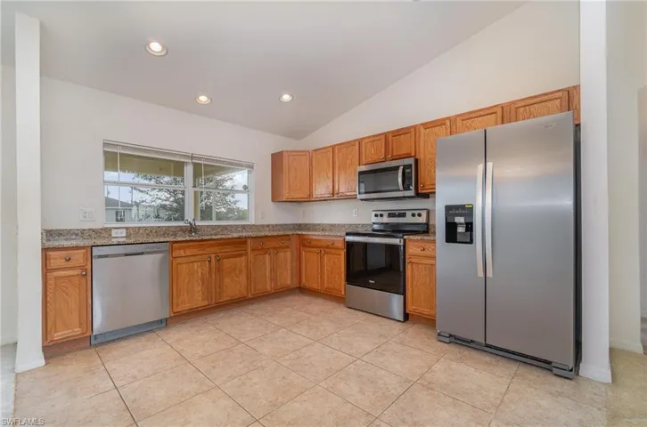 Kitchen with light stone countertops, appliances with stainless steel finishes, vaulted ceiling, sink, and light tile patterned floors