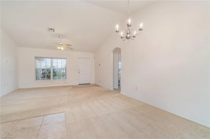 Carpeted empty room with lofted ceiling and ceiling fan with notable chandelier
