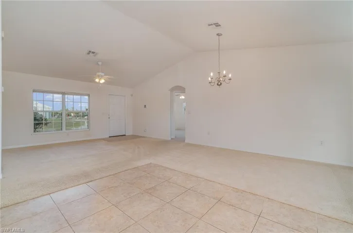 Unfurnished room featuring light tile patterned floors, ceiling fan with notable chandelier, and lofted ceiling
