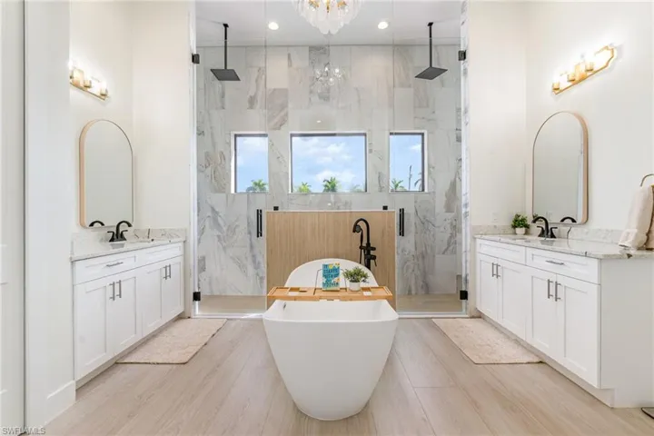 Full bathroom featuring a freestanding bath, a marble finish shower, two vanities, and recessed lighting