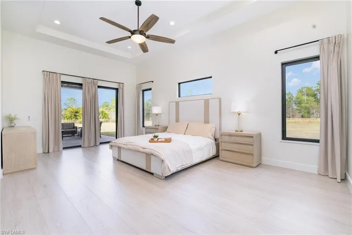 Bedroom with access to exterior, a raised ceiling, ceiling fan, recessed lighting, and light wood-style flooring