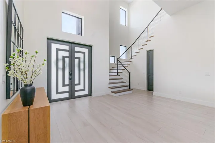 Foyer entrance with a towering ceiling, light wood tile flooring, and wood staircase