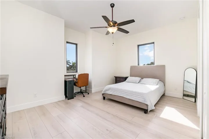 Bedroom with multiple windows, light wood finished floors, a desk, and a ceiling fan