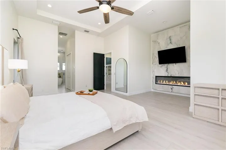 Bedroom featuring recessed lighting, a tray ceiling, a premium fireplace, ceiling fan, and light wood-style floors