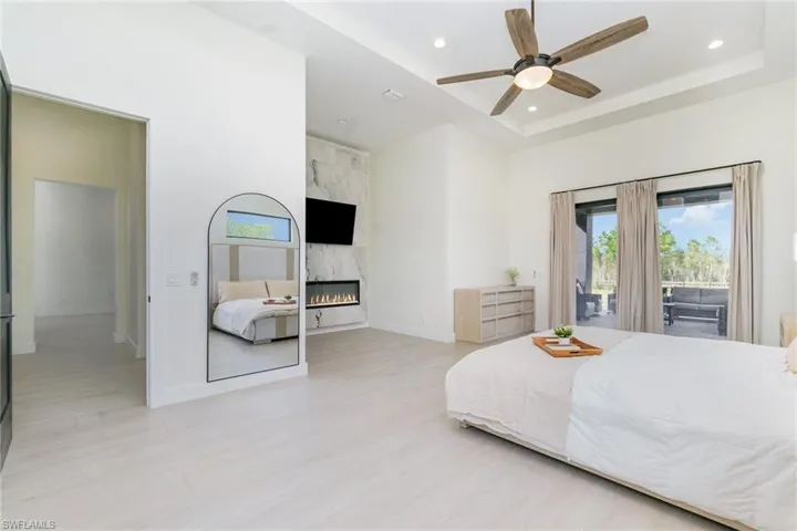Bedroom featuring access to outside, a tray ceiling, a fireplace, light wood-style flooring, and recessed lighting