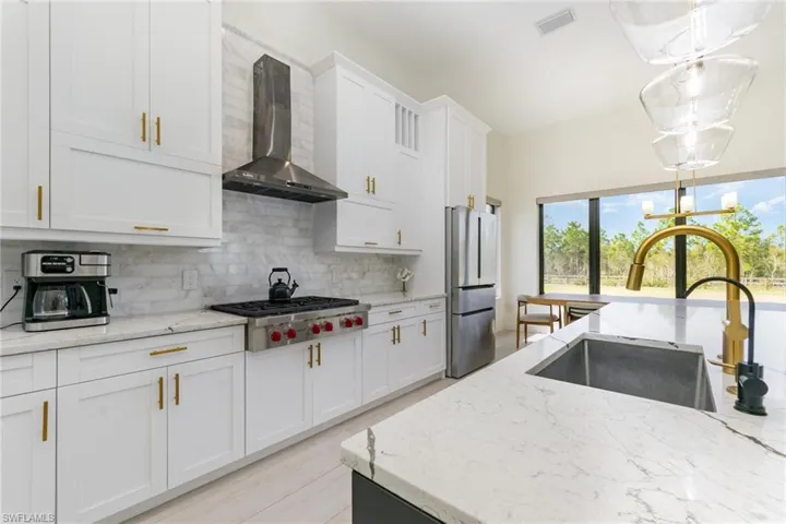 Kitchen featuring light stone countertops, wall chimney exhaust hood, tasteful backsplash, pendant lighting, and white cabinets