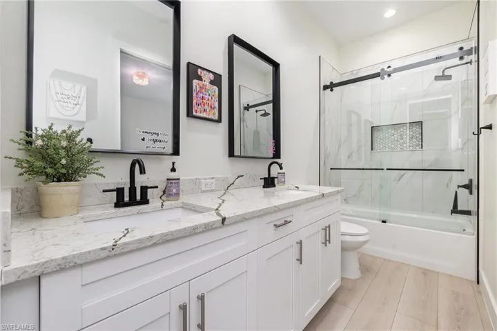 Bathroom with double vanity, enclosed tub / shower combo, and light wood finished floors