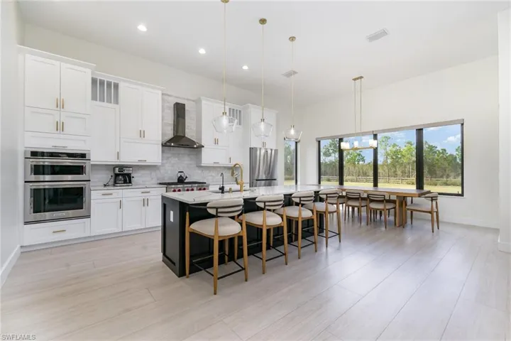 Kitchen with white cabinetry, decorative light fixtures, a kitchen bar, backsplash, and an island with sink
