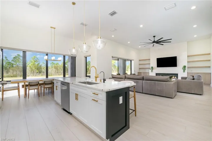 Kitchen with decorative light fixtures, light stone countertops, a kitchen island with sink, white cabinetry, and a kitchen bar