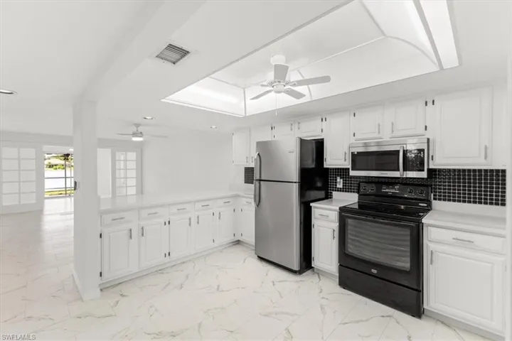 Kitchen with backsplash, appliances with stainless steel finishes, light tile patterned floors, and ceiling fan