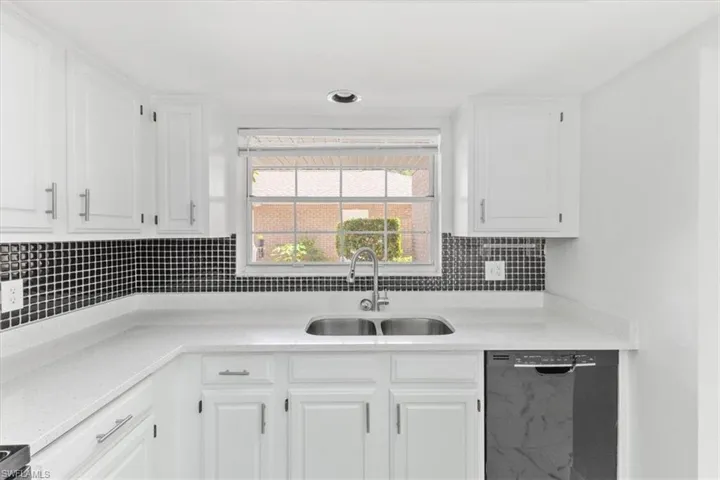 Kitchen with black dishwasher, sink, tasteful backsplash, and white cabinets