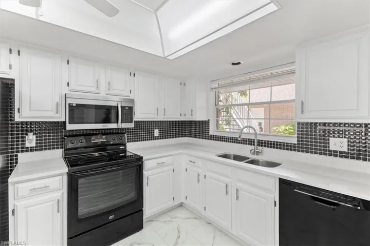 Kitchen featuring white cabinets, light tile patterned floors, black appliances, and sink