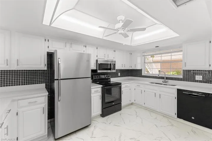 Kitchen featuring white cabinetry, light tile patterned floors, ceiling fan, black appliances, and sink
