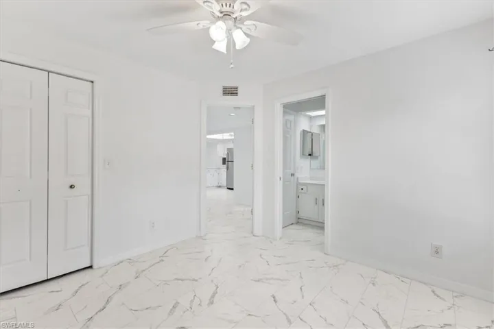 Unfurnished bedroom featuring a closet, ensuite bath, stainless steel refrigerator, light tile patterned flooring, and ceiling fan