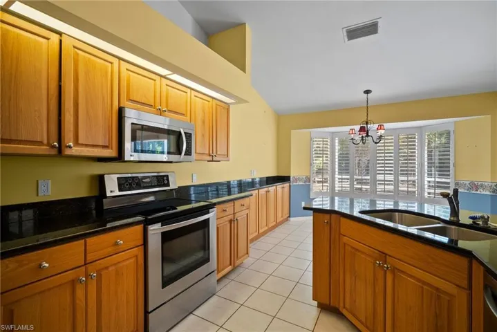 Kitchen with light tile patterned flooring, a sink, visible vents, appliances with stainless steel finishes, and brown cabinets