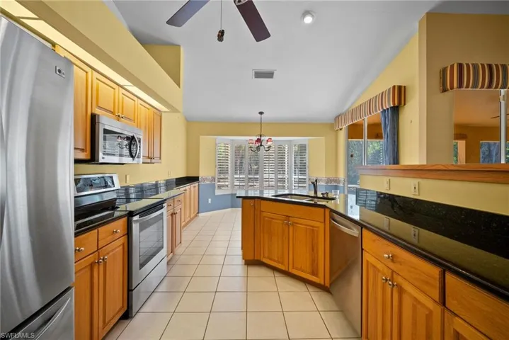 Kitchen with brown cabinets, light tile patterned floors, visible vents, appliances with stainless steel finishes, and a sink