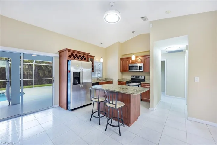 Kitchen featuring stainless steel appliances, light stone counters, lofted ceiling, a breakfast bar, and a kitchen island