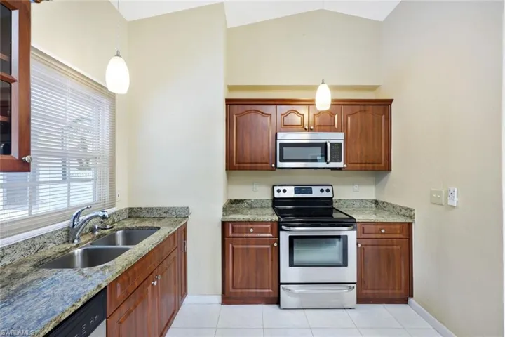 Kitchen featuring stainless steel appliances, light stone countertops, light tile patterned floors, decorative light fixtures, and lofted ceiling