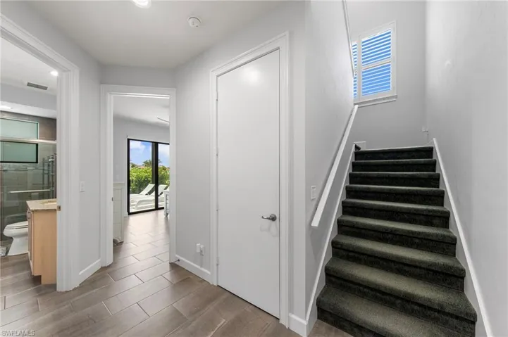 Staircase with dark carpeted treads and white handrail, featuring an upper window with louvered shutters