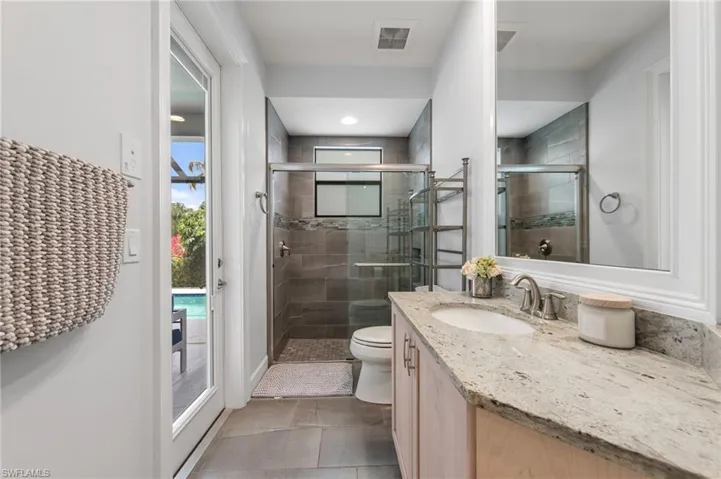Bathroom featuring a single vanity with a light-toned countertop, a frameless shower with a glass enclosure, and a frosted glass door leading to an outdoor area with a pool