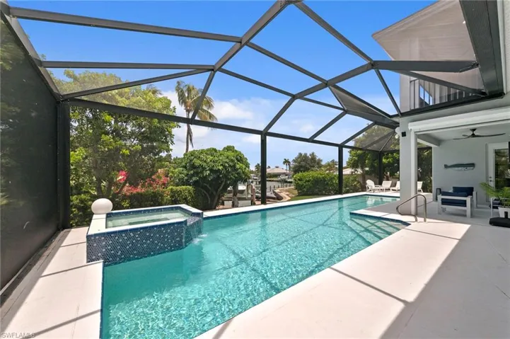 Screen-enclosed pool area featuring a rectangular swimming pool, integrated spa with blue mosaic tile, and concrete decking