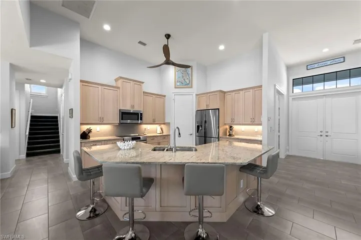 Open-concept kitchen featuring an angled island with seating, recessed lighting, wood cabinetry, and stainless steel appliances