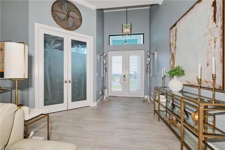 Foyer featuring light tile patterned floors, a high ceiling, ornamental molding, and french doors