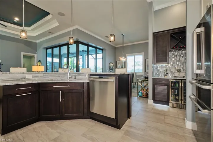 Kitchen with dark brown cabinetry, beverage cooler, sink, crown molding, and stainless steel appliances