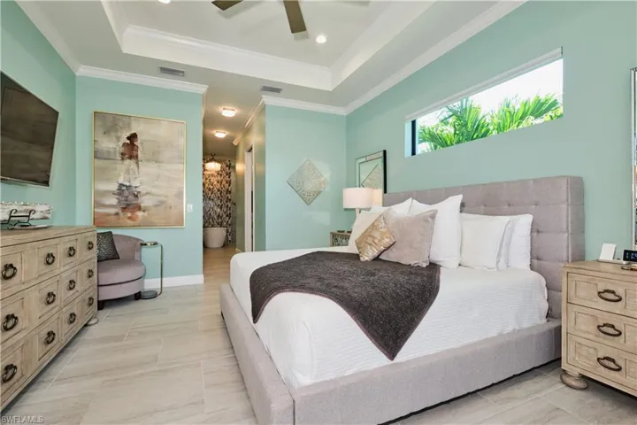 Tiled bedroom featuring ceiling fan, crown molding, and a tray ceiling