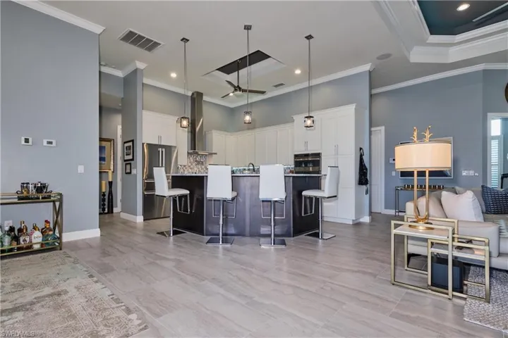 Kitchen with wall chimney exhaust hood, a breakfast bar, white cabinetry, a center island with sink, and stainless steel appliances