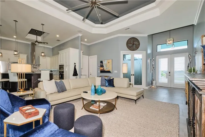 Living room with ceiling fan, crown molding, a raised ceiling, and french doors