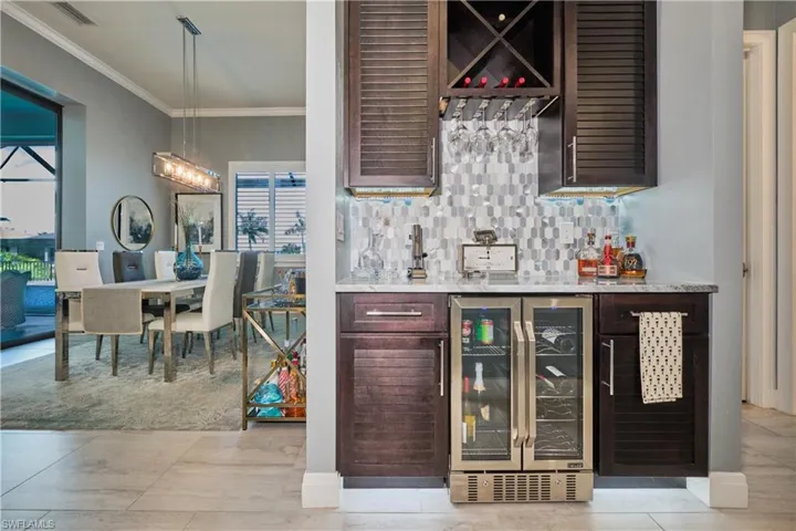 Bar featuring tasteful backsplash, crown molding, pendant lighting, light tile patterned floors, and beverage cooler