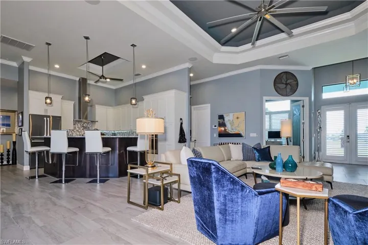 Tiled living room with ceiling fan, a raised ceiling, ornamental molding, a towering ceiling, and french doors