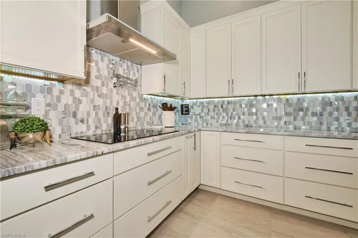 Kitchen featuring black electric cooktop, light stone counters, tasteful backsplash, white cabinetry, and wall chimney range hood