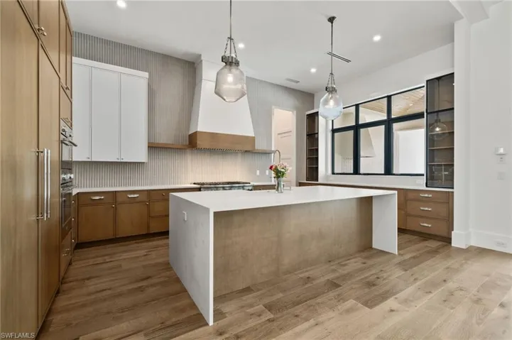 Kitchen with pendant lighting, custom range hood, a kitchen island with sink, tasteful backsplash, and light wood-type flooring