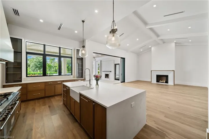 Kitchen with lofted ceiling with beams, light hardwood / wood-style flooring, decorative light fixtures, sink, and a kitchen island with sink