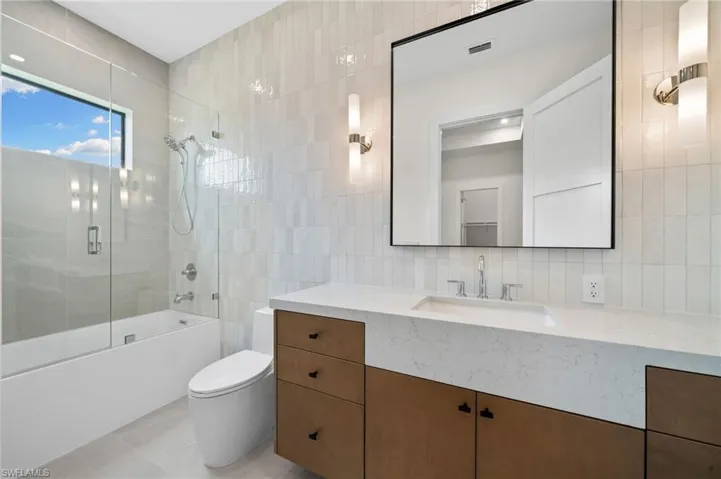 Full bathroom with toilet, vanity, decorative backsplash, enclosed tub / shower combo, and tile walls