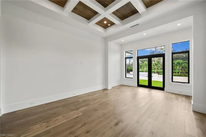 Empty room featuring french doors, coffered ceiling, beamed ceiling, and light hardwood / wood-style flooring